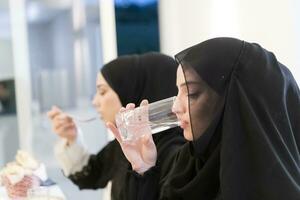 eid Mubarak Muslim Familie haben iftar Abendessen Trinken Wasser zu brechen Fest. Essen traditionell Essen während Ramadan schlemmen Monat beim heim. das islamisch halal Essen und Trinken beim modern Western isla foto