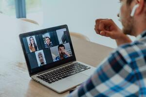 das Mann Sitzung beim ein Tabelle im ein modern Leben Zimmer, mit Kopfhörer mit ein Laptop zum Geschäft Video Plaudern, Konversation mit freunde und Unterhaltung foto