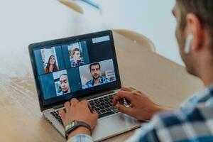 das Mann Sitzung beim ein Tabelle im ein modern Leben Zimmer, mit Kopfhörer mit ein Laptop zum Geschäft Video Plaudern, Konversation mit freunde und Unterhaltung foto