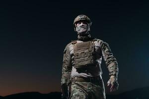 Heer Soldat im Kampf Uniformen mit ein Angriff Gewehr, Teller Träger und Kampf Helm gehen auf ein gefährlich Mission auf ein regnerisch Nacht. foto