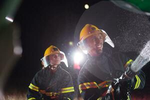 Feuerwehrleute mit ein Wasser Schlauch zu beseitigen ein Feuer Gefahr. Mannschaft von weiblich und männlich Feuerwehrmänner im gefährlich Rettung Mission. foto