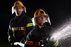 Feuerwehrleute mit ein Wasser Schlauch zu beseitigen ein Feuer Gefahr. Mannschaft von weiblich und männlich Feuerwehrmänner im gefährlich Rettung Mission. foto