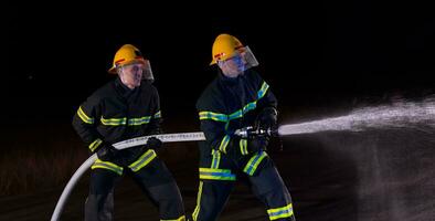 Feuerwehrleute verwenden ein Wasser Schlauch zu beseitigen ein Feuer Gefahr. Mannschaft von Feuerwehrmänner im das gefährlich Rettung Mission. foto