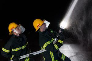 Feuerwehrleute verwenden ein Wasser Schlauch zu beseitigen ein Feuer Gefahr. Mannschaft von Feuerwehrmänner im das gefährlich Rettung Mission. foto