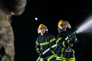 Feuerwehrleute mit ein Wasser Schlauch zu beseitigen ein Feuer Gefahr. Mannschaft von weiblich und männlich Feuerwehrmänner im gefährlich Rettung Mission. foto