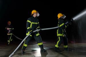 Feuerwehrleute mit ein Wasser Schlauch zu beseitigen ein Feuer Gefahr. Mannschaft von weiblich und männlich Feuerwehrmänner im gefährlich Rettung Mission. foto