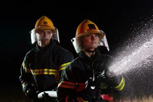 Feuerwehrleute mit ein Wasser Schlauch zu beseitigen ein Feuer Gefahr. Mannschaft von weiblich und männlich Feuerwehrmänner im gefährlich Rettung Mission. foto