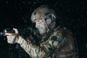 Heer Soldat im Kampf Uniformen mit ein Angriff Gewehr, Teller Träger und Kampf Helm gehen auf ein gefährlich Mission auf ein regnerisch Nacht. foto