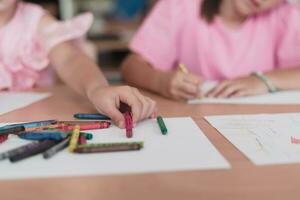 wenig Mädchen Sitzung im elementar Schule Zeichnung auf Papier mit ihr freunde während Sitzung im ein modern Klassenzimmer foto