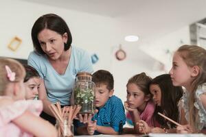 weiblich Lehrer mit Kinder im Biologie Klasse beim elementar Schule Dirigieren Biologie oder botanisch wissenschaftlich Experiment Über nachhaltig wachsend Pflanzen. Lernen Über Pflanzen im ein Glas Krug foto