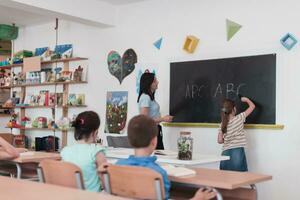 elementar Schule. das weiblich Lehrer Portion das Kind Schüler während Schreiben das Antworten auf das Tafel. foto