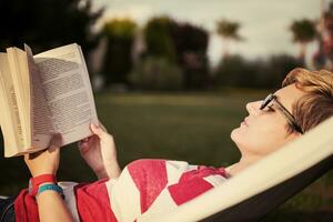 Frau, die ein Buch liest, während sie sich auf der Hängematte entspannt foto