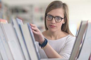 Porträt einer Studentin, die ein Buch zum Lesen in der Bibliothek auswählt foto