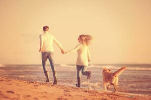 Paar mit Hund, das sich am Herbsttag am Strand amüsiert foto