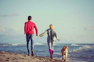 Paar mit Hund, das sich am Herbsttag am Strand amüsiert foto