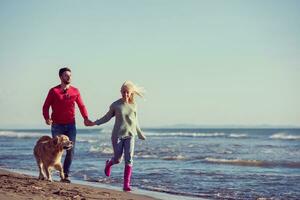 Paar mit Hund, das sich am Herbsttag am Strand amüsiert foto