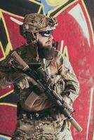 ein bärtig Soldat im ein Besondere Kräfte Uniform steht im Vorderseite von ein gezeichnet Mauer mit ein Gewehr im seine Hand. selektiv Fokus foto