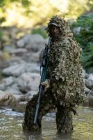 ein Militär- Mann oder Airsoft Spieler im ein tarnen passen schleichen das Fluss und Ziele von ein Scharfschütze Gewehr zu das Seite oder zu Ziel. foto