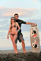 Surf-Paar posiert am Strand bei Sonnenuntergang foto