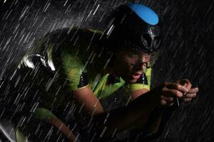 Triathlon-Athlet, der in regnerischer Nacht schnell Fahrrad fährt foto