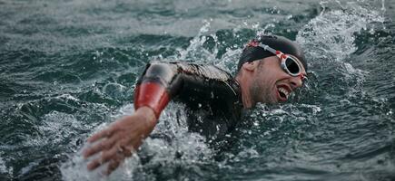 Triathlon-Athlet, der bei Sonnenaufgang auf dem See schwimmt und einen Neoprenanzug trägt foto