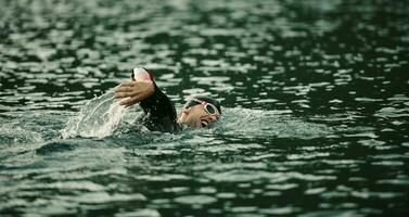 Triathlon-Athlet, der bei Sonnenaufgang auf dem See schwimmt und einen Neoprenanzug trägt foto