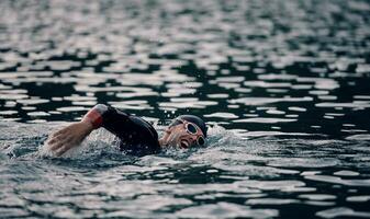 Triathlon-Athlet, der bei Sonnenaufgang auf dem See schwimmt und einen Neoprenanzug trägt foto