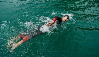 Triathlon-Athlet, der auf dem See schwimmt und einen Neoprenanzug trägt foto