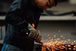 schwerindustrie-fabrikinnenraum mit industriearbeiter, der winkelschleifer verwendet und ein metallrohr schneidet. Auftragnehmer in der Herstellung von Metallstrukturen für Sicherheitsuniformen und Schutzhelme. foto