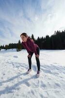 Junge Frau, die im Freien auf Schnee im Wald joggt foto