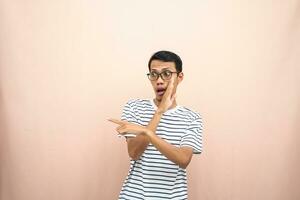 asiatisch Mann mit Brille tragen beiläufig gestreift Shirt, Flüstern Pose während zeigen zu das Seite. isoliert Beige Hintergrund. foto