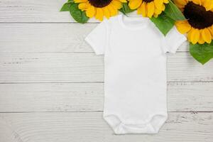 Weiß Baby Mädchen oder Junge Bodysuit Attrappe, Lehrmodell, Simulation eben legen mit Sonnenblumen auf Weiß hölzern Hintergrund. Design Strampler Vorlage, drucken Präsentation spotten hoch. oben Sicht. foto