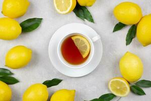 Tasse von Tee mit frisch Zitronen und Blätter auf Licht grau Beton Hintergrund. heiß gesund Getränk. immun Verteidigung, Vitamin c. oben Sicht. foto