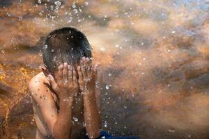 asiatisch jung Junge süß und charmant spielen Wasser im das Fluss auf das Hintergrund von Grün Reis Felder und Sonnenaufgänge, Kind spielen Wasser, thailändisch Kinder- Lebensstil, glücklich, Spaß, Freude. foto