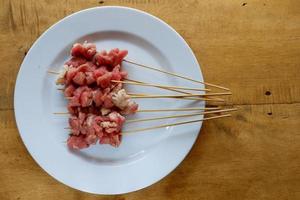 Roher Ziegen-Satay auf weißem Teller mit Holztisch foto