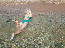 ein blondes Mädchen, das auf dem Bauch im durchsichtigen Meerwasser liegt foto
