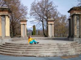 lächelndes Mädchen, das auf der Treppe des Parks sitzt und die Frühlingssonne schaut foto