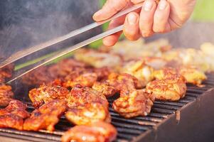 Kochen Hähnchen Flügel auf das Feuer. ein des Mannes Hand flippt Flügel auf ein Grill. Picknick, Straße Lebensmittel. foto