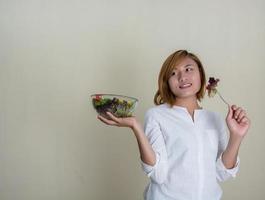 schöne Frau, die eine Schüssel Salat hält und etwas Gemüse isst foto