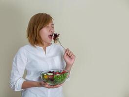 schöne Frau, die eine Schüssel Salat hält und etwas Gemüse isst foto