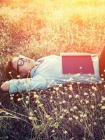 junge Hipster-Frau, die im Blumenfeld liegt, nachdem sie zum Lesen müde war foto