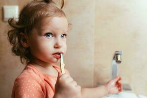 süß und komisch Baby Mädchen Bürsten ihr Zähne im das Morgen im das Bad foto