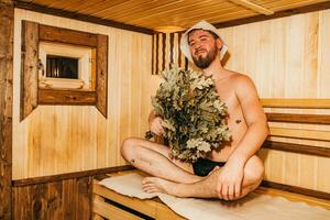 ein Mann mit ein Besen im seine Hand ist entspannend im das Sauna foto