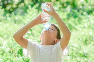 süß Kind Getränke Wasser von ein Flasche auf das Straße im Sommer- foto