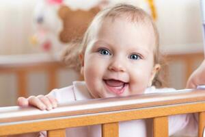 Porträt von ein Lachen Mädchen Wer steht im ein Krippe im das Zimmer foto