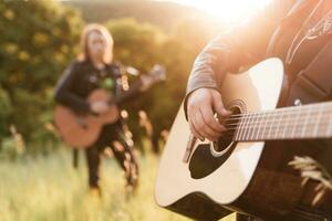 Frau und Mann spielen akustisch Gitarre im Natur beim Sonnenuntergang foto