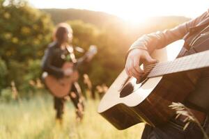 Frau und Mann spielen akustisch Gitarre im Natur beim Sonnenuntergang foto