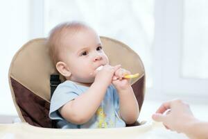 Baby halten ein Löffel im seine Mund foto