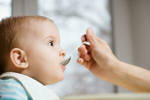 Mutter gibt Baby Essen von ein Löffel foto