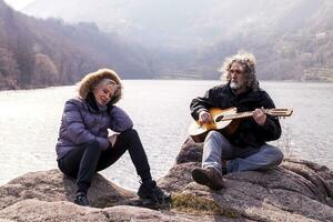 schön reifen Paar spielen ein Gitarre Sitzung auf das See foto